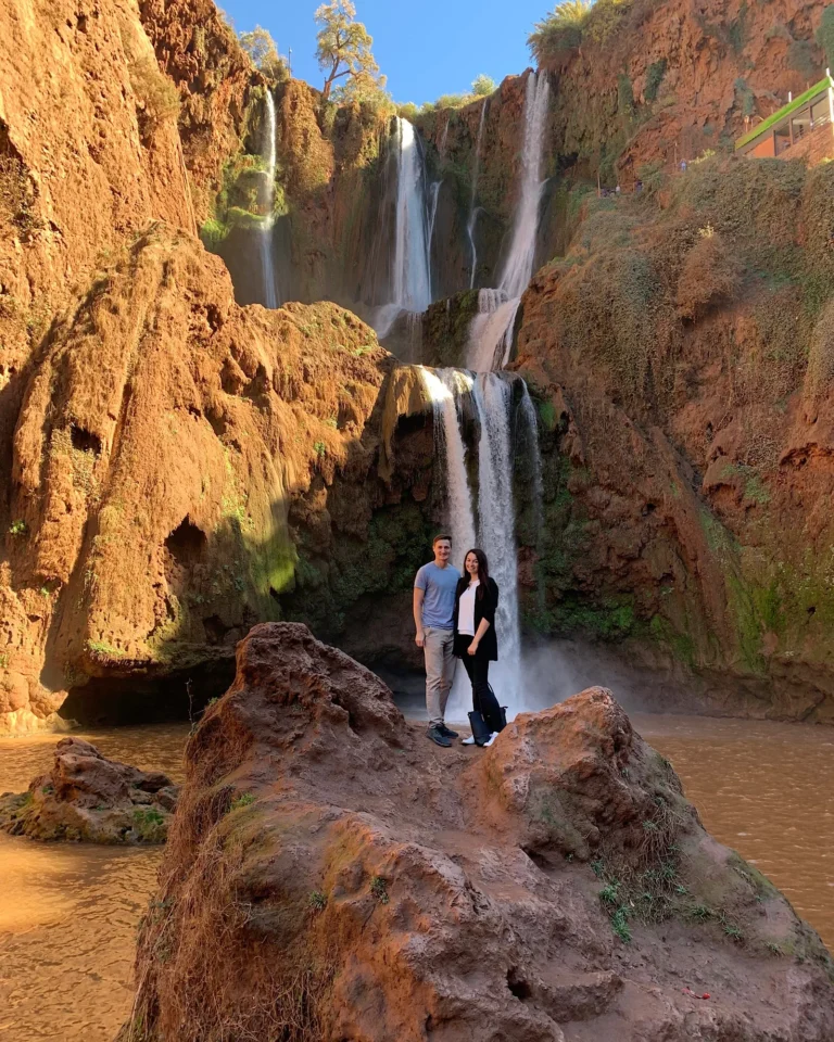 Young travel couple standing in front of Ouzoud Waterfalls in sunny weather.
