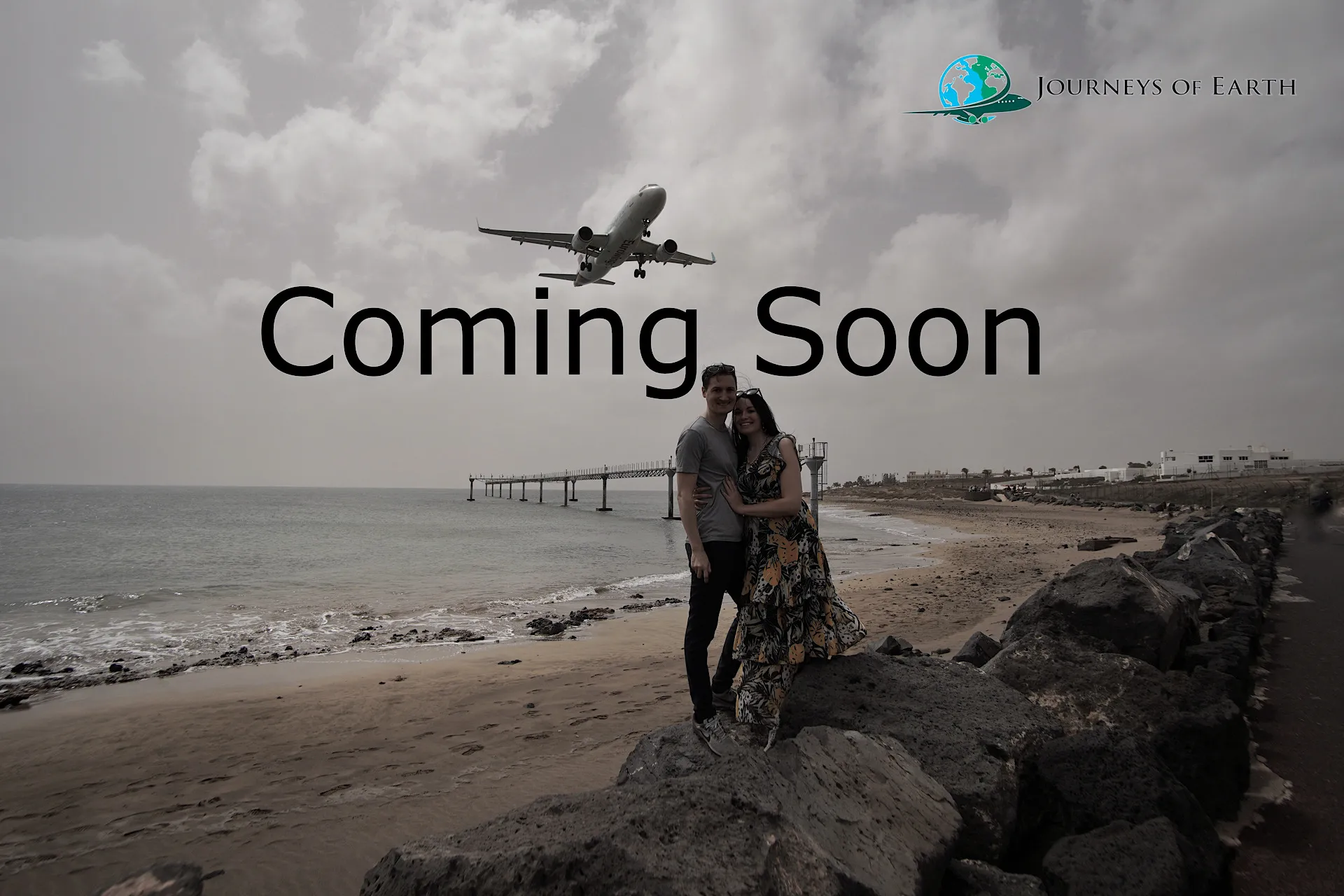 Travel couple standing on a beach in Lanzarote directly under a low-landing airplane.