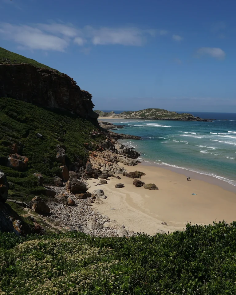 View of a prominent green mountain, yellow sand, and blue ocean at Robberg Nature Reserve.