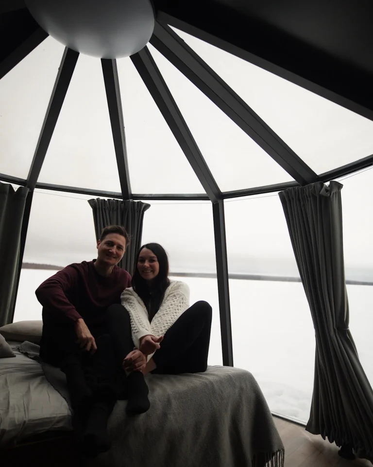 A couple sitting on a bed inside an glass igloo in Rovaniemi.