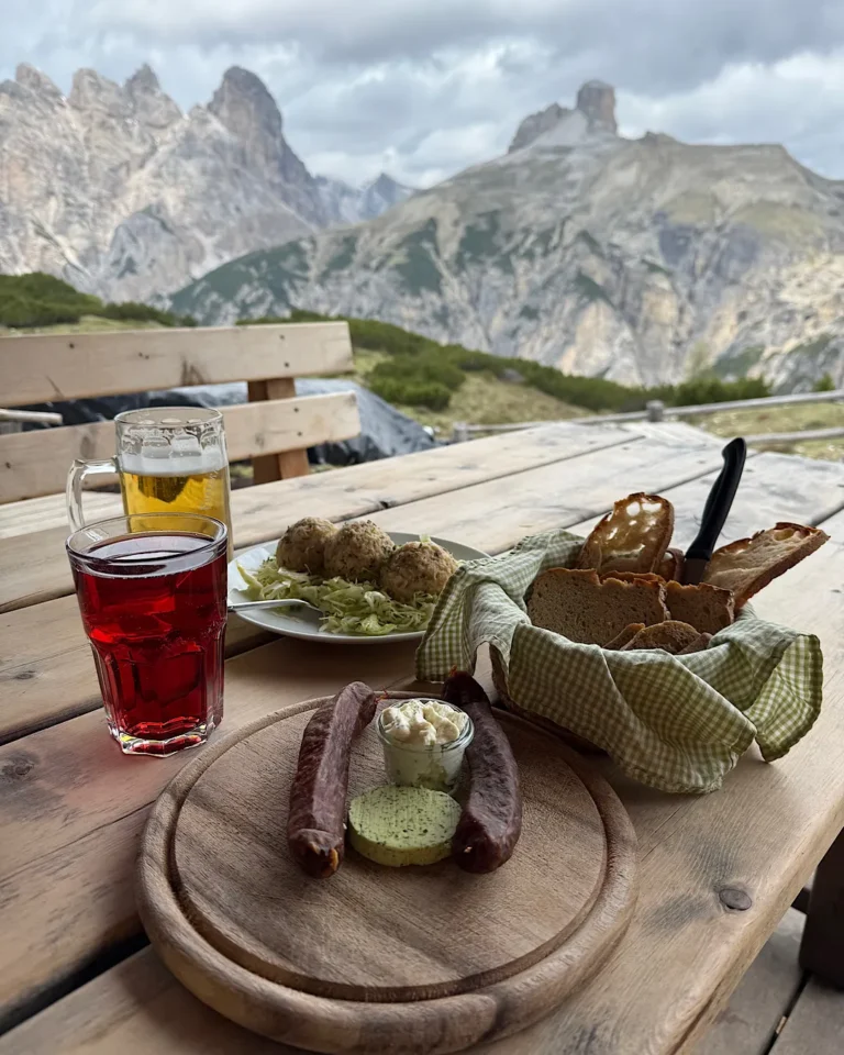 Traditional South Tyrolean meal with dumplings, sausages, and bread on a wooden table overlooking the mountains.