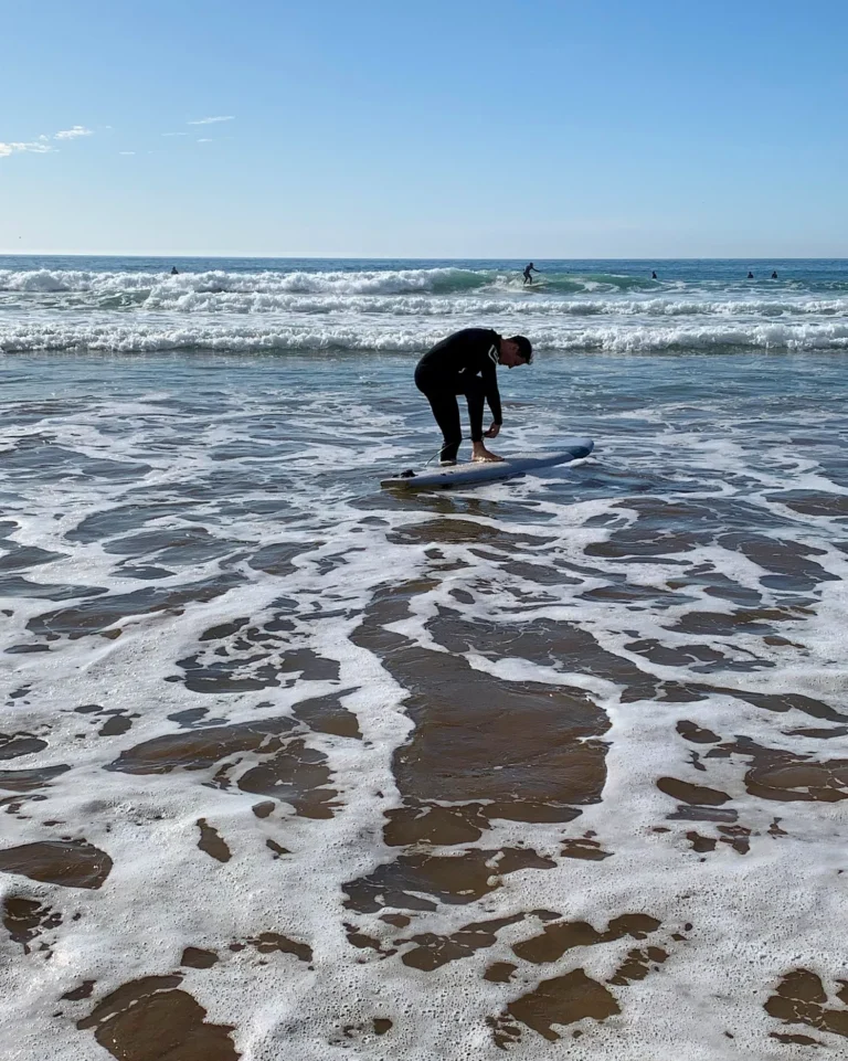 Surfer standing with his board in shallow water at Agadir beach.