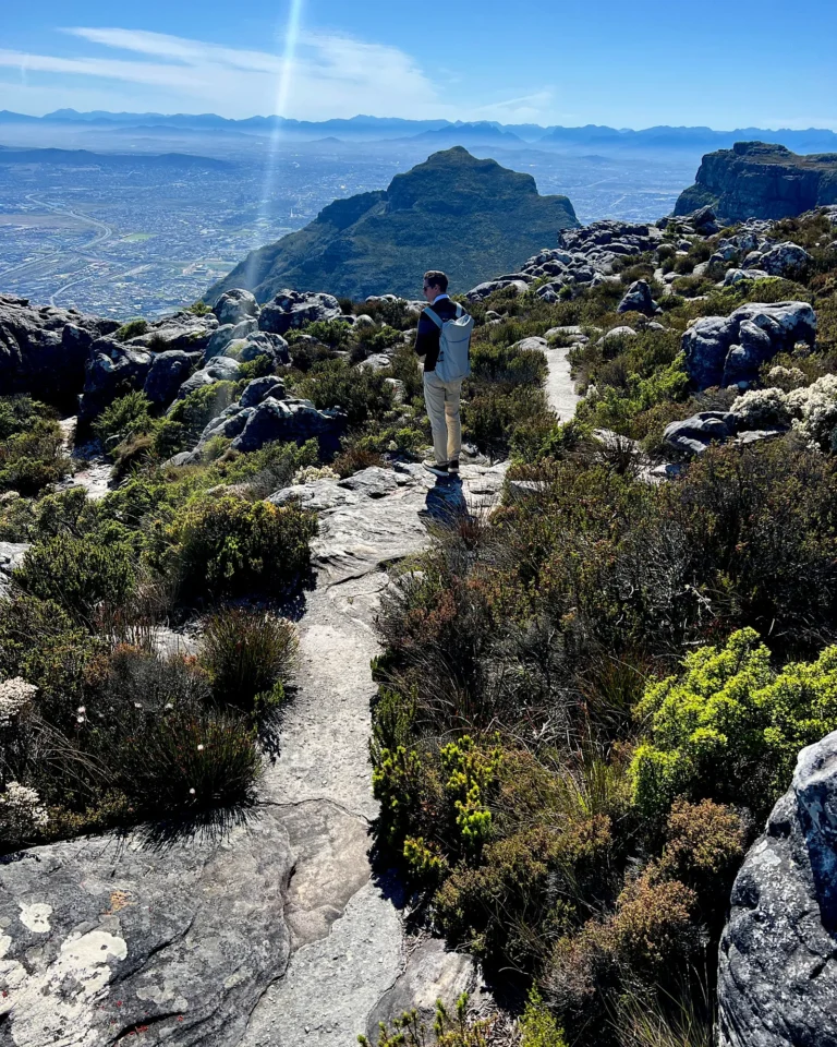 Young man with a backpack standing on a rocky hiking trail at the summit of Table Mountain.
