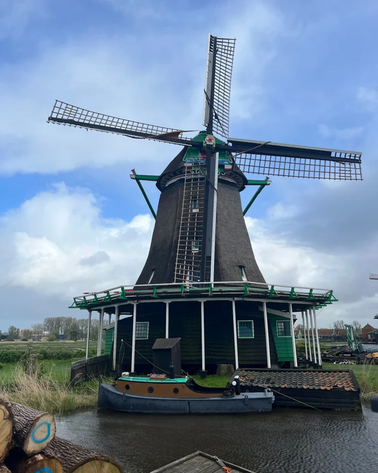Eine traditionelle grüne Windmühle im Freilichtmuseum Zaanse Schans steht im Vordergrund des Bildes.