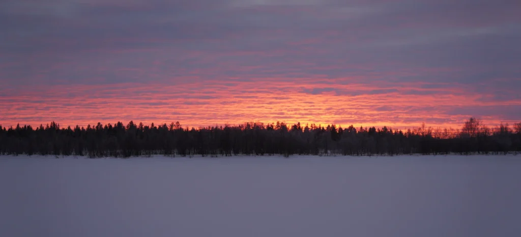 Brennender roter Himmel über einem verschneiten See und Winterwald in Enontekiö, Finnisch-Lappland.