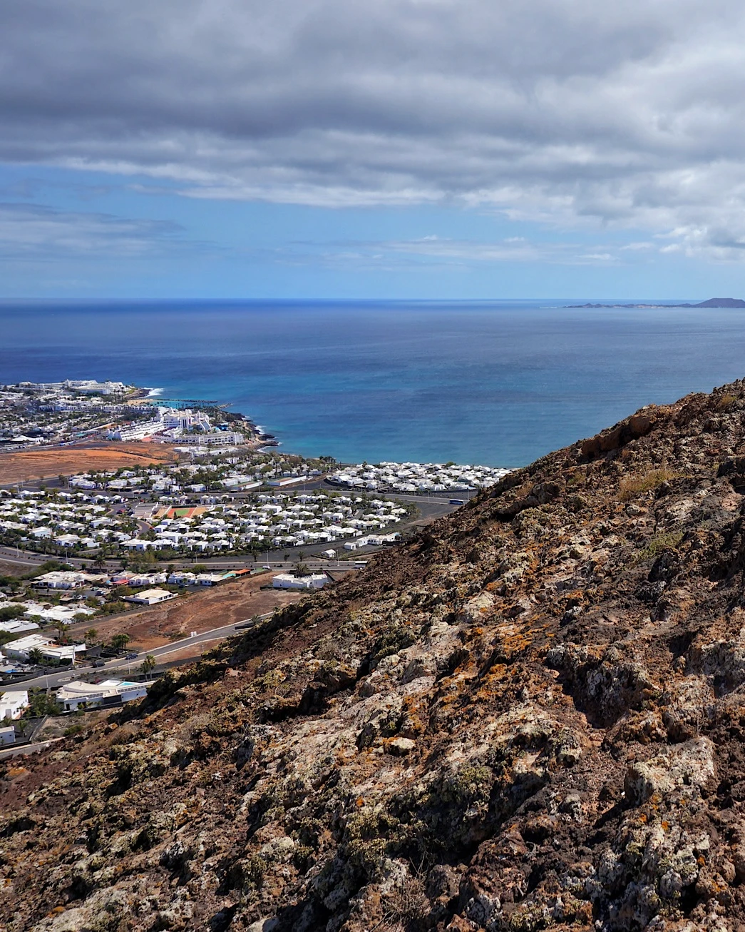View from Montaña Roja overlooking the ocean and a white village in Lanzarote during a hike.