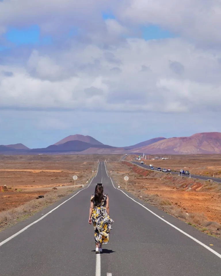 Woman in a blowing yellow dress walking on a road through the lava fields in Timanfaya National Park.